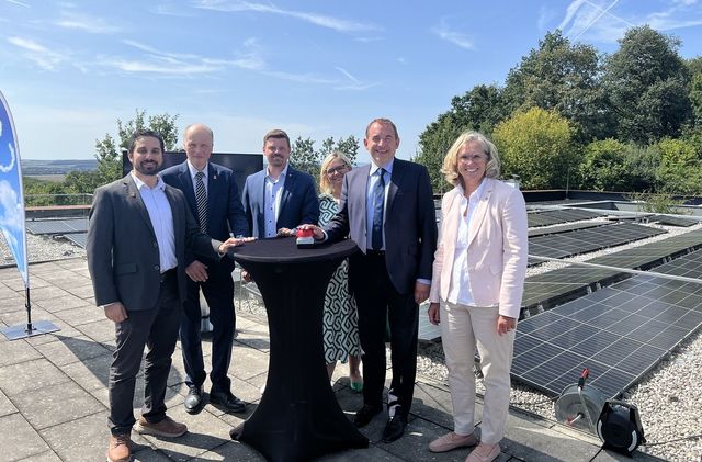 Hessens Finanzminister Professor Dr. R. Alexander Lorz (2. v. r.) steht mit 5 weiteren Personen an einen Tisch und drückt symbolisch einen Startknopf; im Hintergrund ist eine Photovoltaikanlage zu sehen